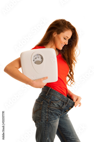 Beautiful young woman holding scale and too big trousers as she