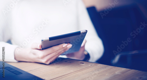 Closeup view of young businesswoman using digital tablet at the wooden table.Concept coworking people work with mobile devices.Horizontal, blurred background.Film effect.
