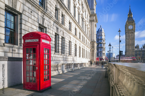 London, England - Traditional red british telephone box with Big Ben and Double Decker bus at the background on a sunny afternoon with blue sky and clouds