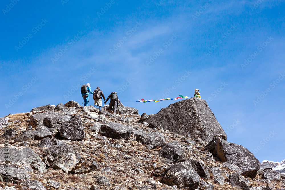 Group of Mountain Climbers approaching to rocky Summit with buddhist Flags