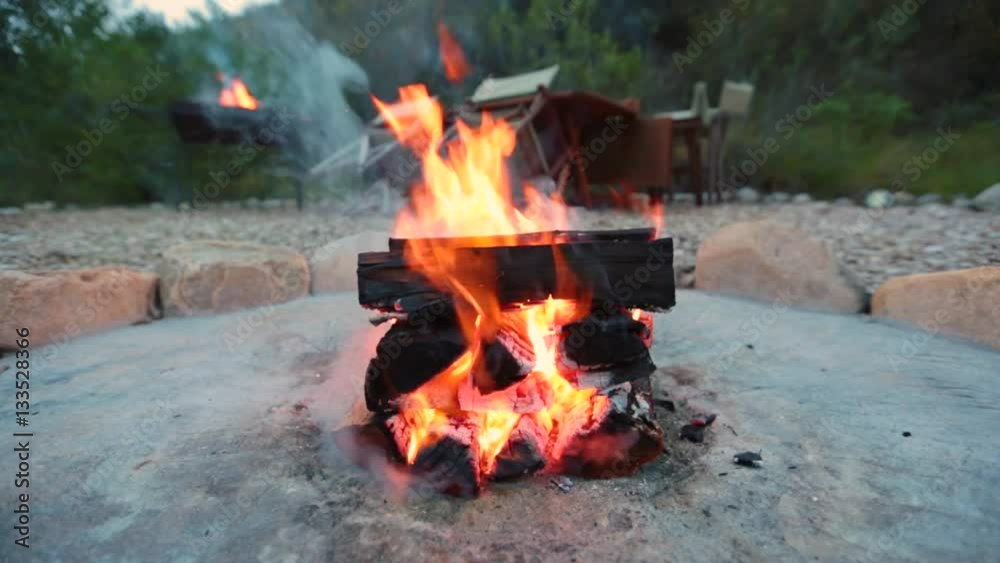A campfire burns in a fire pit at a safari camp with another in the