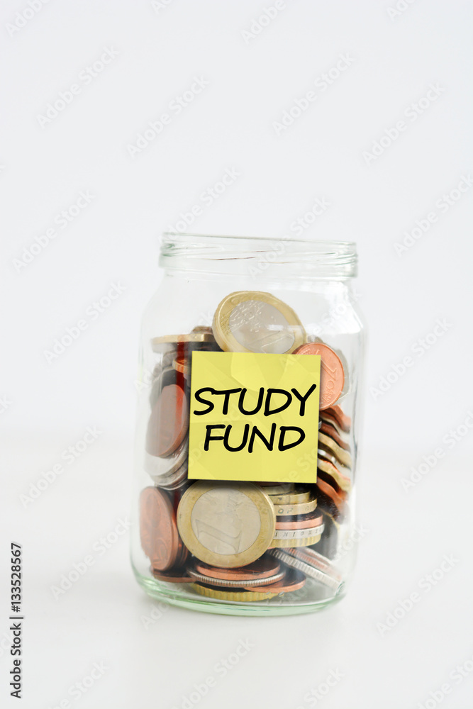 A lot of coins stacked in a glass jar labeled study fund A lot of coins stacked in a glass jar labeled study fund