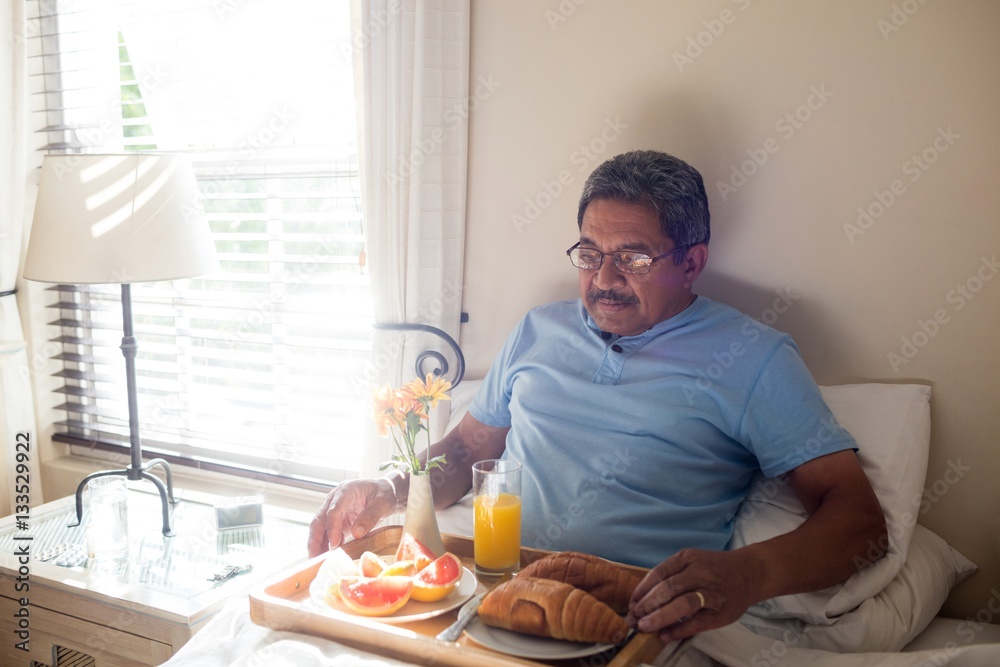 Senior man having breakfast on bed