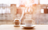 Coffee cup and cupcake on wooden table in morning,soft focus.