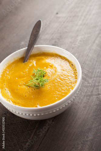 Close up of small white bowl of Spiced Pumpkin Soup on top of wooden background