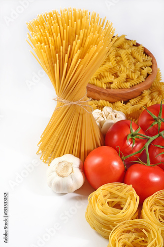 Uncooked Italian pasta, ripe tomatoes branch and garlic on a whi