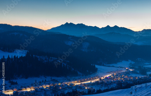 Twilight over the Tatra Mountains with the illuminated village in the valley.
