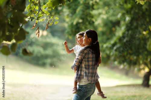 Mother holding her daughter and playing around the park on beautiful morning.