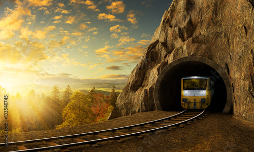 Mountain railroad with train in tunnel in rock above landscape.