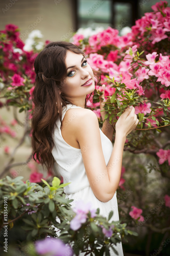 Beautiful brunette woman in flower garden with red pink azalea in a sensual dress Beautiful brunette woman in flower garden with red pink azalea in a sensual dress
