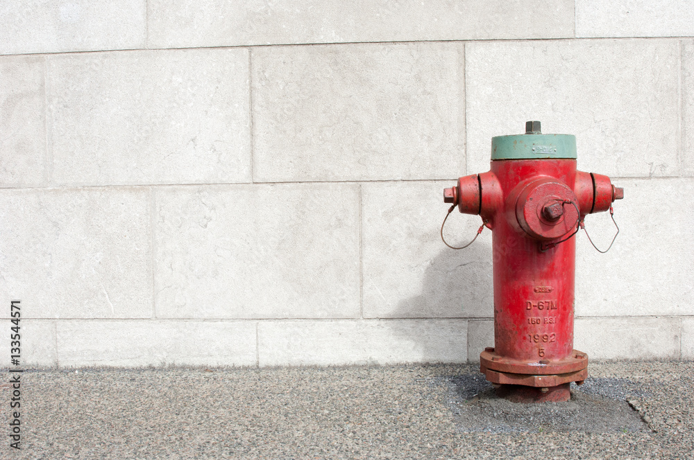 Red and green fire hydrant next to a light concrete wall on the sidewalk in Montreal, Quebec, Canada. Copy space on the left. Red and green fire hydrant next to a light concrete wall on the sidewalk in Montreal, Quebec, Canada. Copy space on the left.