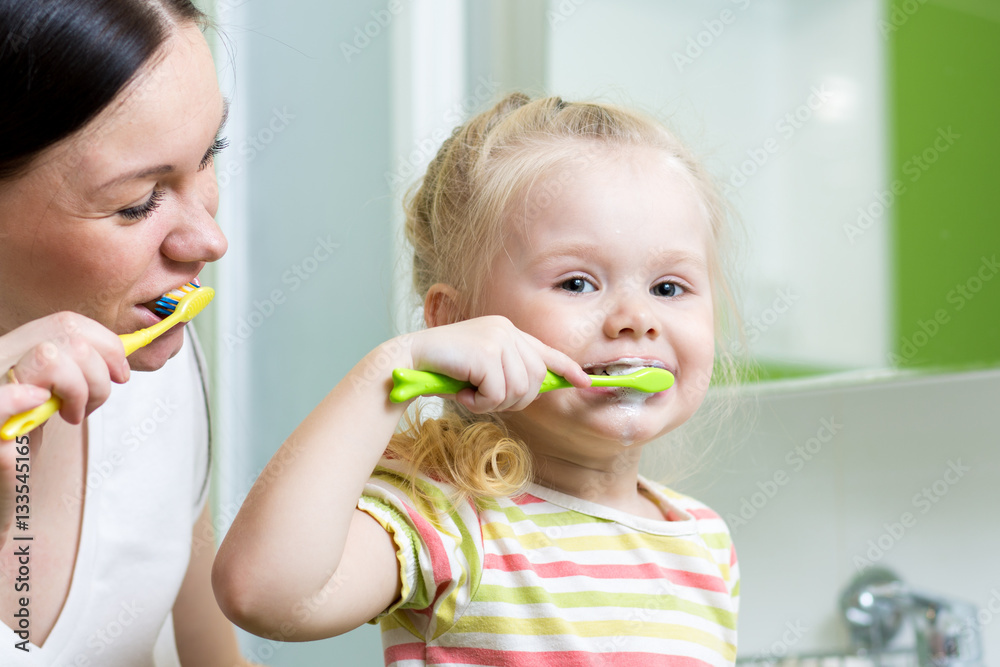 mother and little daughter brushing teeth in bathroom mother and little daughter brushing teeth in bathroom