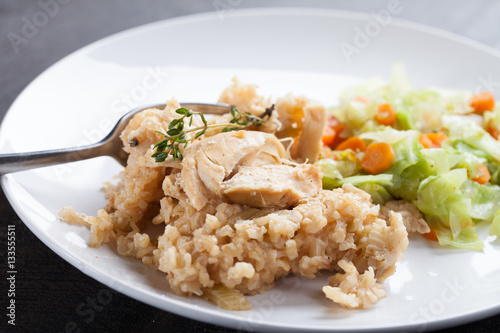 Lemon pepper chicken on brown rice with steamed carrots and cabbage on a dark wooden background horizontal shot