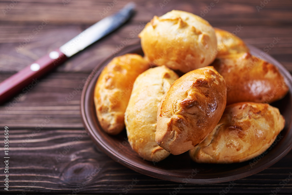 Delicious rustic pastries filled with meat and vegetables on a ceramic plate with wooden knife on a wooden background. Delicious rustic pastries filled with meat and vegetables on a ceramic plate with wooden knife on a wooden background.