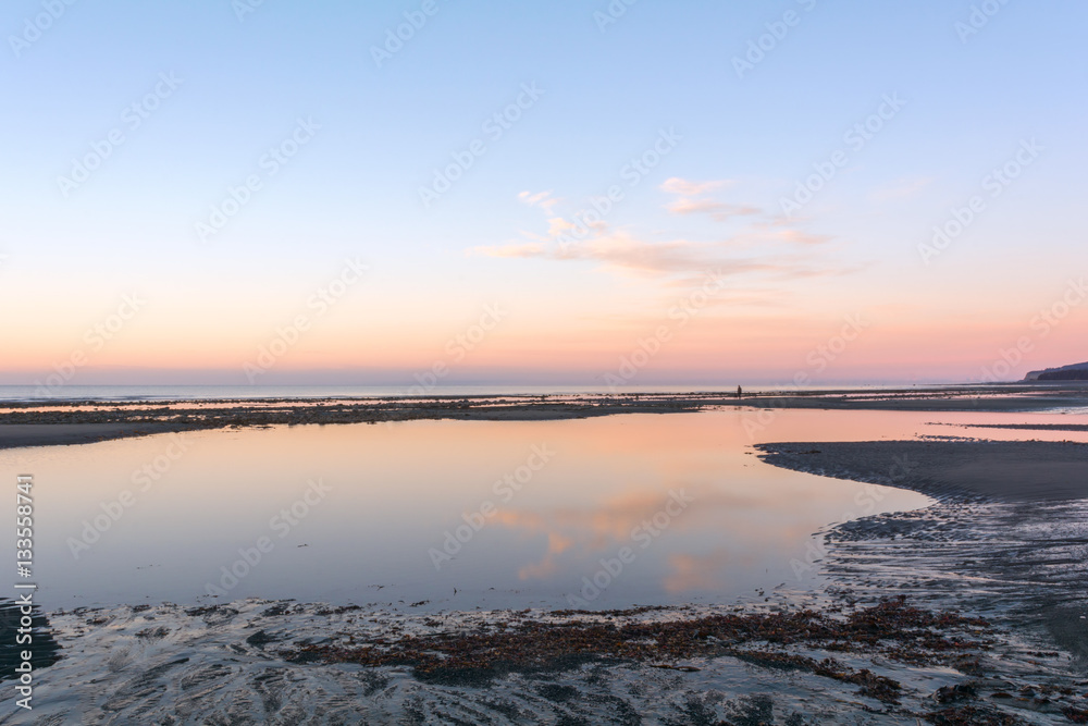 Pre dawn light is reflected in pink on a tidal pool on a Homer Alaska beach.