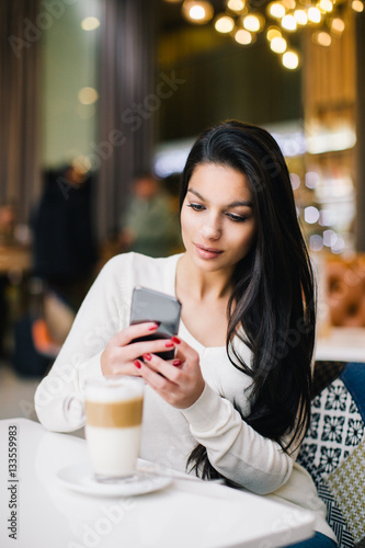 Young woman at cafe drinking coffee and using mobile phone 