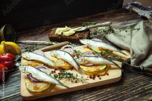 Fresh fish with aromatic herbs, spices, salt, onion rings, bread, bottles with olive oil and balsamic vinegar,perch on cracker, on dark vintage background, top view, healthy food