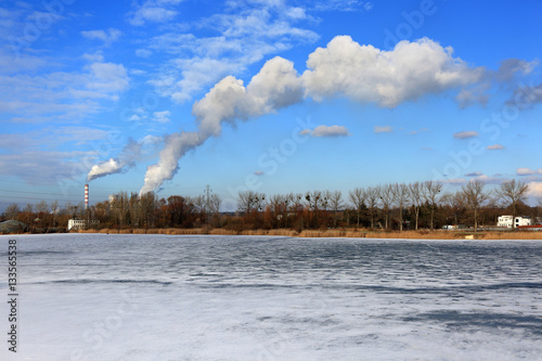 Krajobraz zimowy, dymiące kominy elektrowni, zamarznięte jezioro.