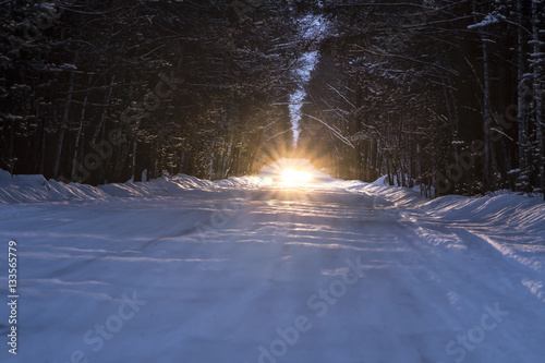car headlights shine on winter snowy road at night in forest
