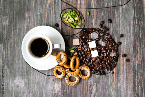 Coffee cup, coffee beans, cardamon seeds, dried biscuits, sugar cubes on wooden table. Top view.