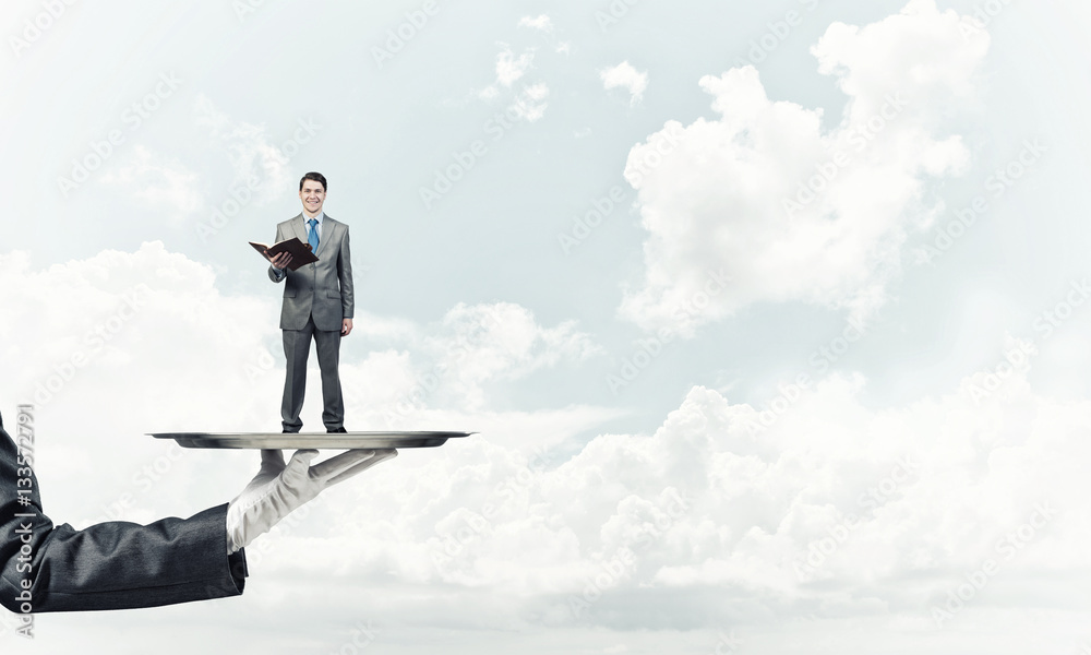 Businessman on metal tray with red book in hands against blue sky background Businessman on metal tray with red book in hands against blue sky background