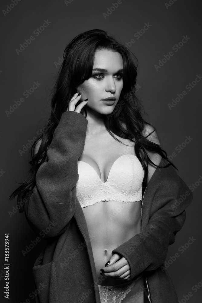 Naklejka premium Black and white photo of a seductive brunette girl in studio. Sexy woman in white lingerie. Monochrome image.