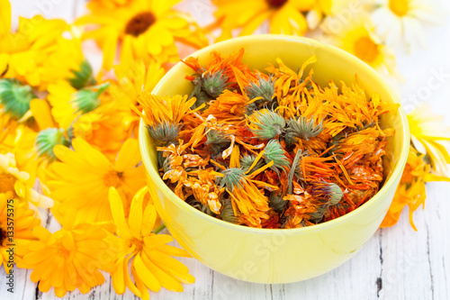 Fresh and dried calendula flowers on white wooden background