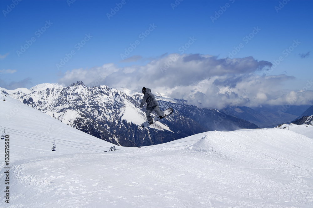Snowboarder jumping in terrain park at snow mountain on sun wint