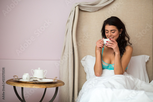 Woman in bed with cup. Young female indoor. My morning starts from coffee.