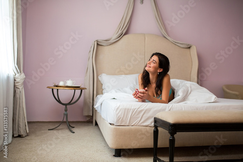 Lady lying and holding cup. Smiling woman in bedroom. My weekend starts from coffee. © DenisProduction.com