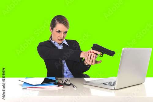 фотографія businesswoman pointing gun to computer laptop sitting at office isolated green c