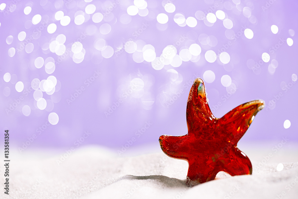 red Glass star fish on beach sand and festive glitter background red Glass star fish on beach sand and festive glitter background
