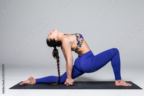 Anjanejasana.  Beautiful yoga woman practice yoga poses on grey background. Yoga concept. photo