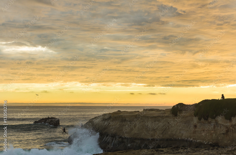 Obraz premium Surfer jumps off cliff into ocean at sunset in California