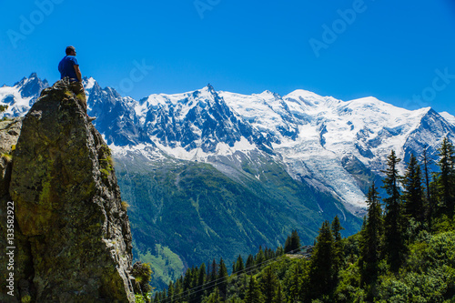 Hiker perched on a stone spire looks out at the French Alps and Mont Blanc above Chamonix, France photo