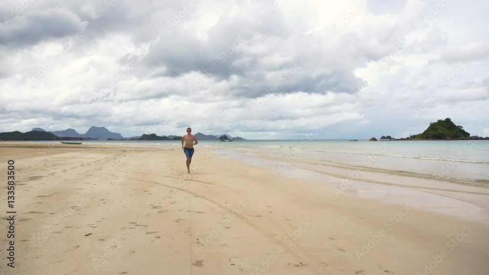 Man running along beach. Fitness sports runner man jogging on beach. Handsome young fit sporty male athlete running outside on beautiful beach training. 4K video. Man running along beach. Fitness sports runner man jogging on beach. Handsome young fit sporty male athlete running outside on beautiful beach training. 4K video.