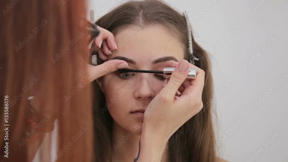 Close up shot. Professional make-up artist applying mascara on eyelashes of model in white room. Beauty, makeup and fashion concept Close up shot. Professional make-up artist applying mascara on eyelashes of model in white room. Beauty, makeup and fashion concept