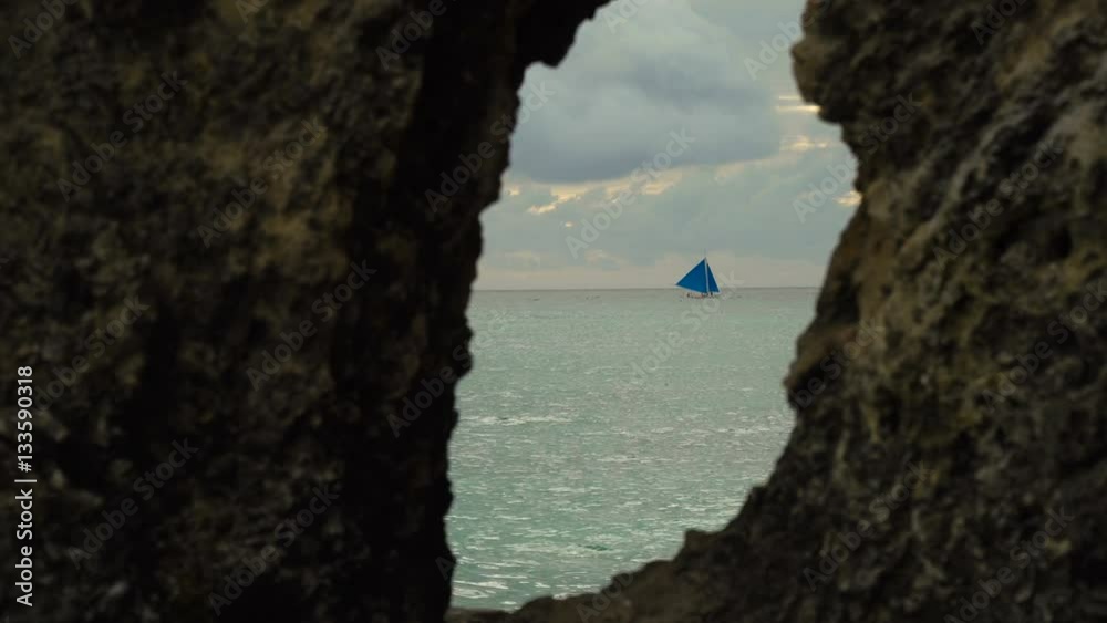 Sailing boat view through a hole in the rock. Sailing ship yachts with blue sails in the ocean. Sail boat on sea. Philippines, Boracay. 4K video. Travel concept. Sailing boat view through a hole in the rock. Sailing ship yachts with blue sails in the ocean. Sail boat on sea. Philippines, Boracay. 4K video. Travel concept.