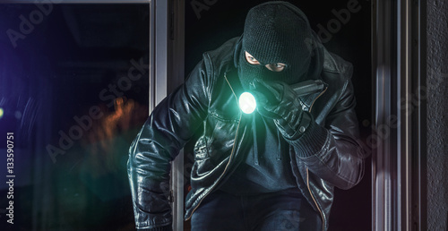 Einbrecher mit Brecheisen und Taschenlampe im Fenster eines Hauses
