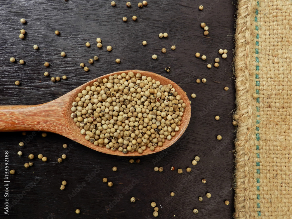 White pepper in wooden ladle on old wooden table and sackcloth background White pepper in wooden ladle on old wooden table and sackcloth background