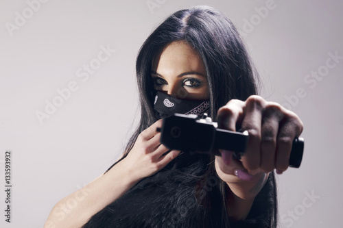 Beautiful brunette woman with a pistol pointing to camera, wearing a bandana  as a thief, looking menacing. Over a grey background. Stock Photo | Adobe  Stock