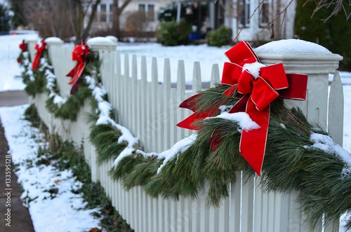 Snow covered evergreen garland draped along a white picket fence