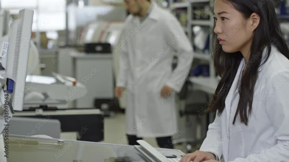 Tilt up of concentrated Asian woman in lab coat operating SMT machine at factory Tilt up of concentrated Asian woman in lab coat operating SMT machine at factory
