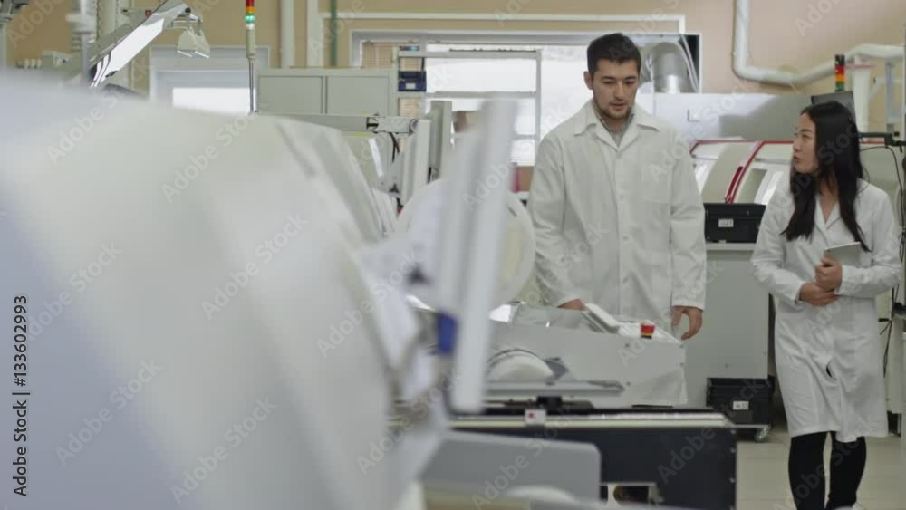 Two colleagues in lab coats walking around SMT factory and speaking about manufacturing machines Two colleagues in lab coats walking around SMT factory and speaking about manufacturing machines