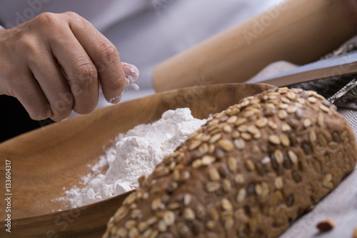 Whole grain bread put on kitchen napkin decorated with almond with a chef holding dough roller at the background.