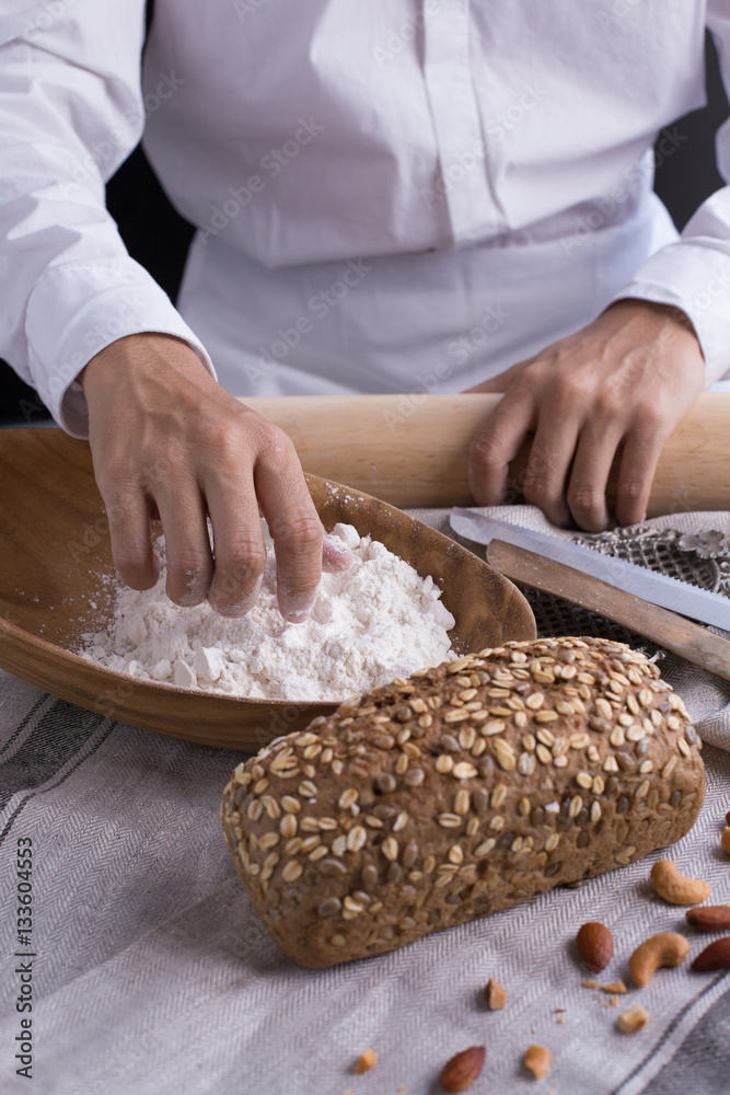 Whole grain bread put on kitchen napkin decorated with almond with a chef holding dough roller at the background. Whole grain bread put on kitchen napkin decorated with almond with a chef holding dough roller at the background.