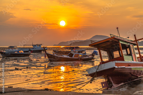 golden sky in Rawai beach fishing boats are parking on the mug 