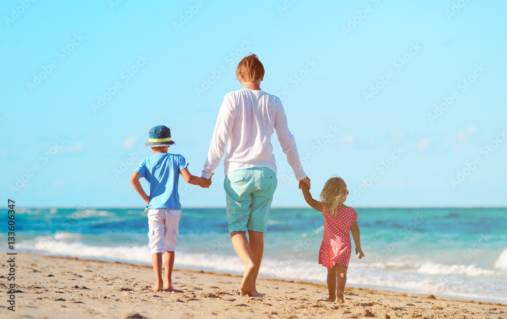 father and two kids walking on beach