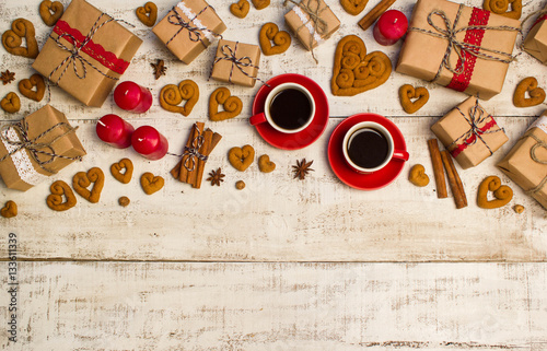 Two red coffee cups, gifts, cookies in the shape of a heart on a white wooden background