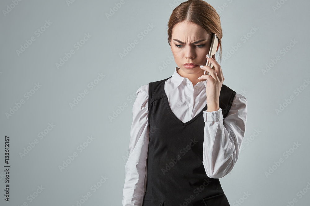 Young girl talking at the cellphone on a gray background